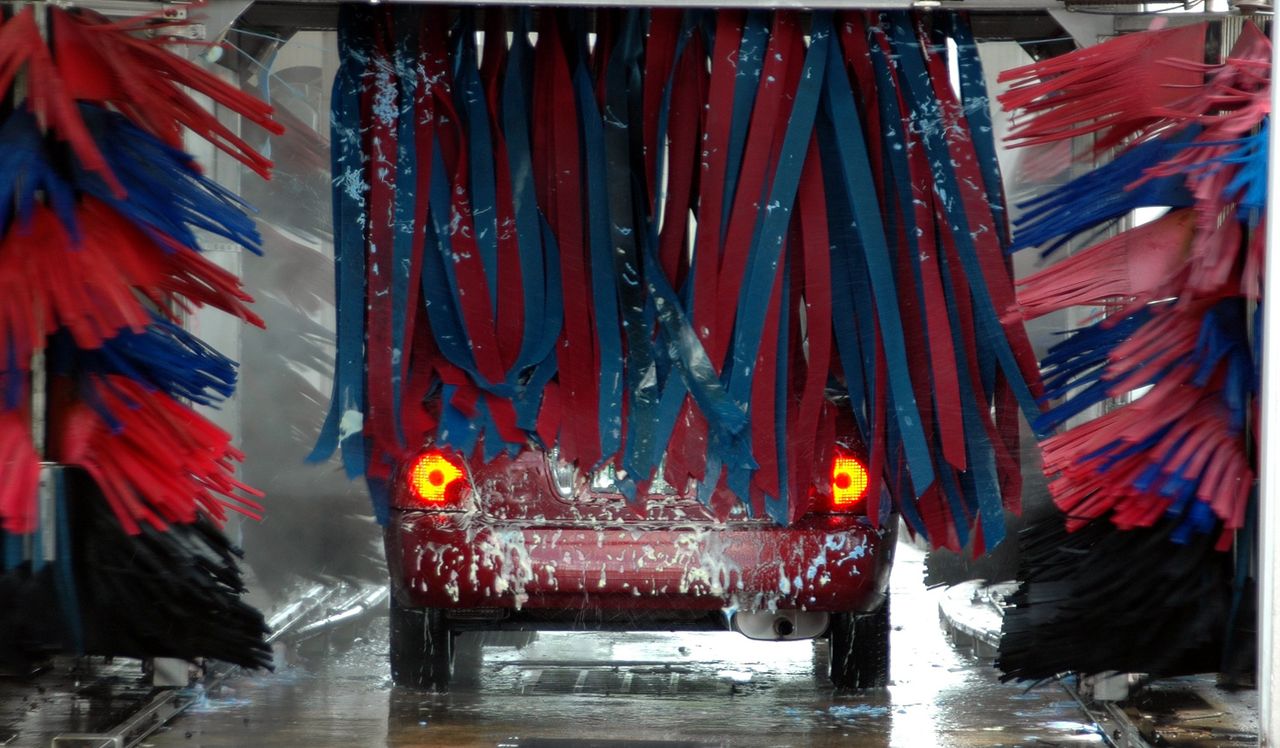 Overcoming Challenges Lessons Every Entrepreneur Must Learn Red car being cleaned in an automated car wash with colorful brushes and soap suds.